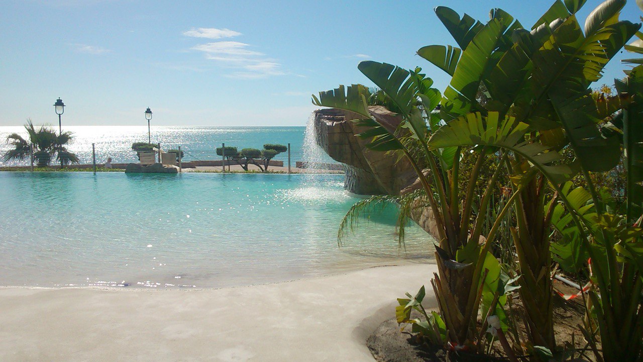 Piscina playa junto al mar con cascada y vegetación tropical